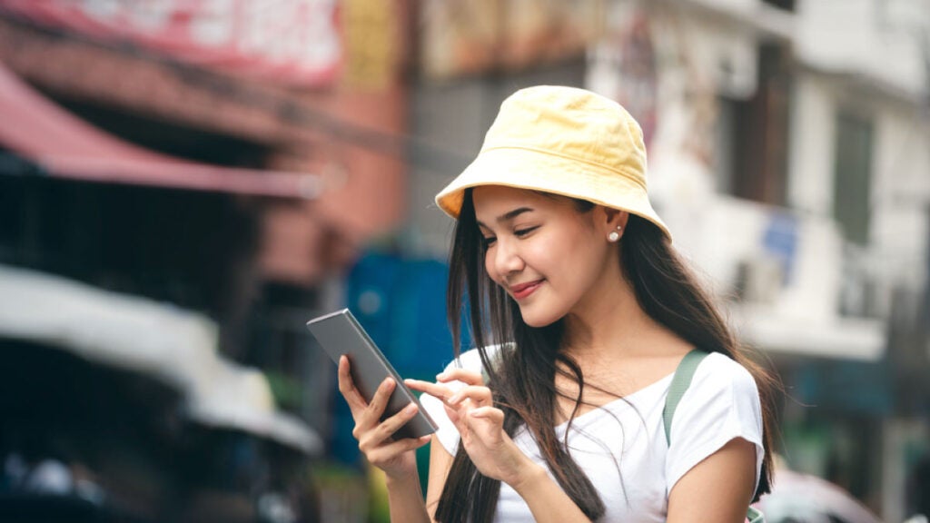 タイの街中でスマートフォンを操作する若い女性旅行者