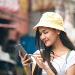 タイの街中でスマートフォンを操作する若い女性旅行者