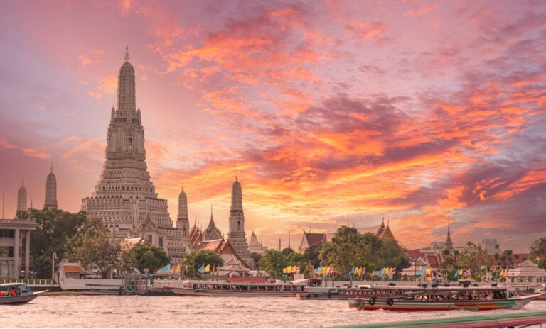 夕焼け空の下に立つタイ・バンコクのワット・アルンとチャオプラヤー川に浮かぶボートの風景