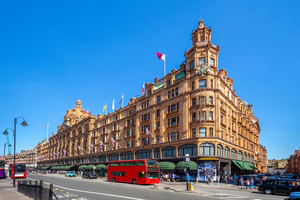 ロンドンの老舗デパート「ハロッズ」と赤い2階建てバスの街並みを紹介する写真。