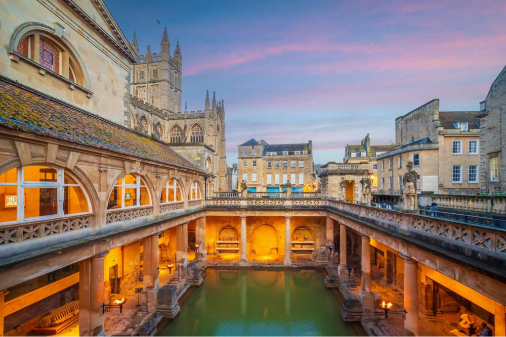 夕暮れ時にライトアップされたローマ浴場と背景にそびえるバース寺院の風景
