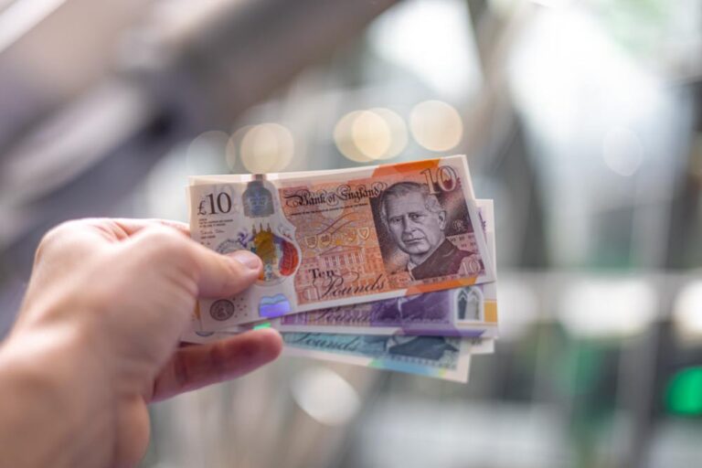 チャールズ国王の肖像が印刷されたイギリスの紙幣を手に持つ写真。
