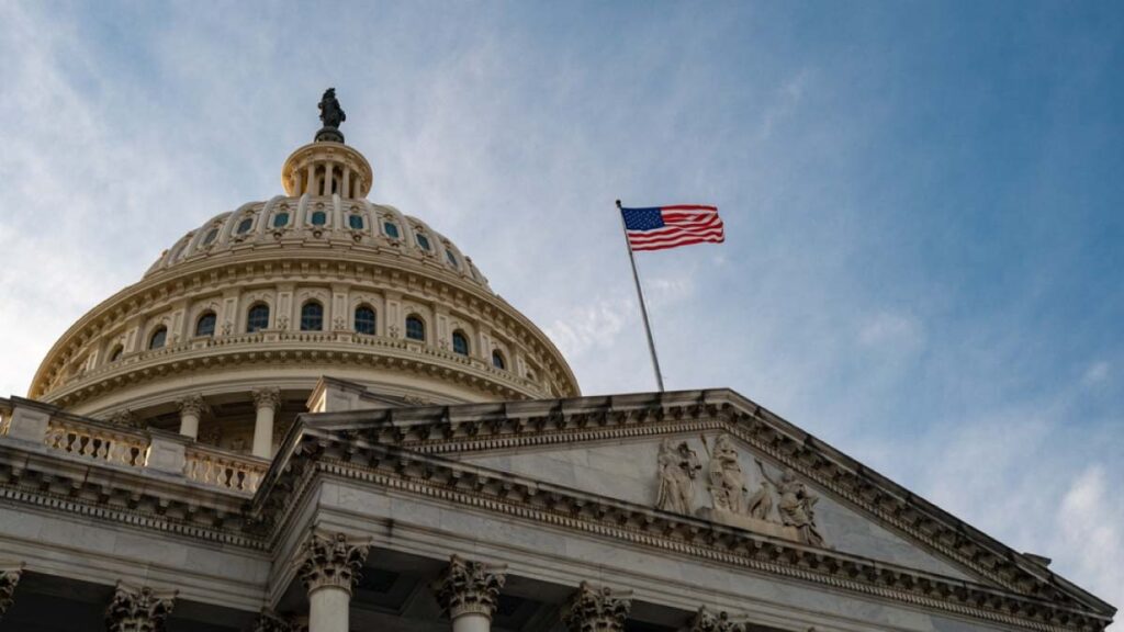 アメリカ国旗が掲げられた米国連邦議会議事堂のドームとファサードを見上げる構図。