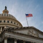 アメリカ国旗が掲げられた米国連邦議会議事堂のドームとファサードを見上げる構図。