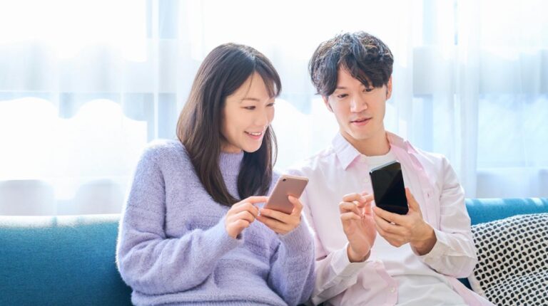 ソファに座ってスマートフォンを操作する笑顔の男女
