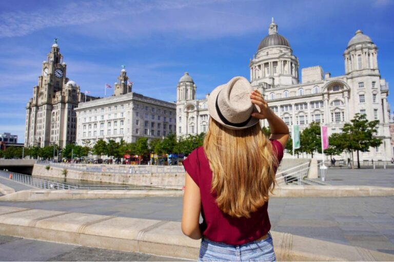 リバプールの三美神を見上げる旅行者。帽子を右手でおさえた女性がウォーターフロントの歴史的建築を眺める後ろ姿。