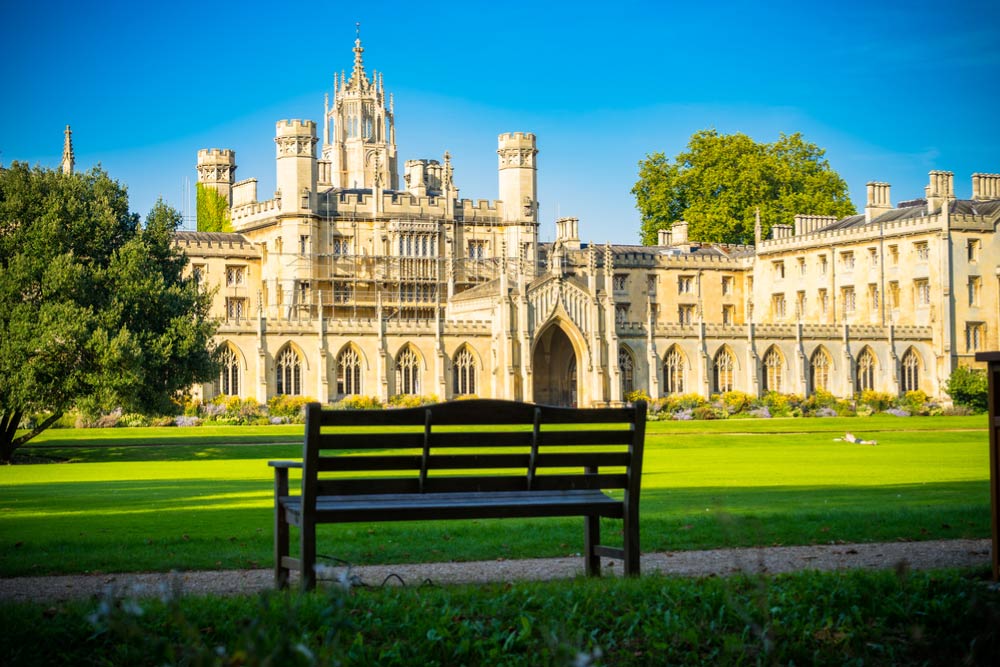 ケンブリッジ大学トリニティ・カレッジの壮麗な校舎と芝生の中庭を写した写真。ベンチ越しに見える歴史的建築が、静かな学びの空間を感じさせる。
