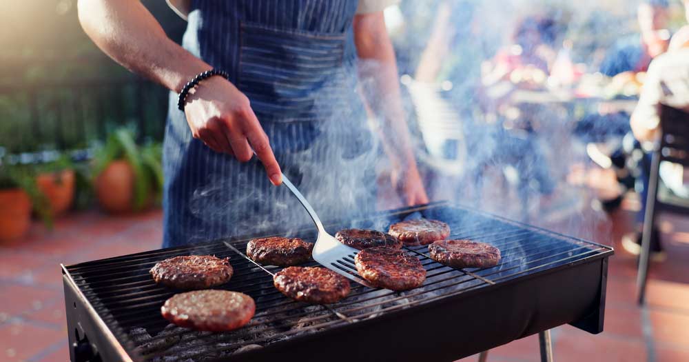 オーストラリアの屋外BBQでオージービーフのパティを焼いている様子。煙が立ちのぼり、仲間と楽しむ本場のBBQ文化を感じられるシーン。