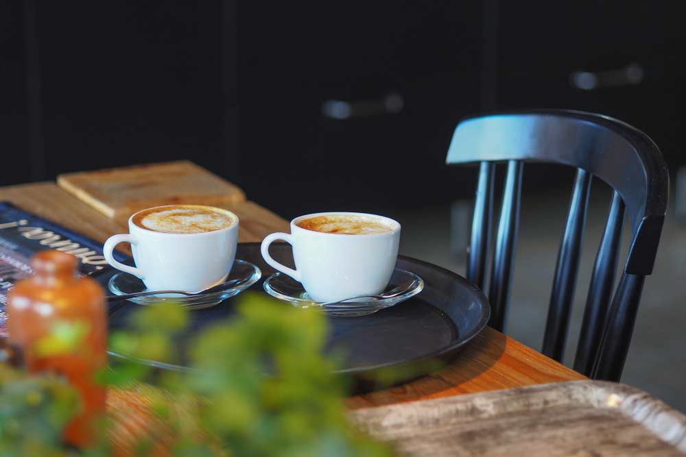 メルボルンのカフェ文化を象徴する一場面。木のテーブルに置かれた2杯のラテが、温かみのある雰囲気を演出している写真