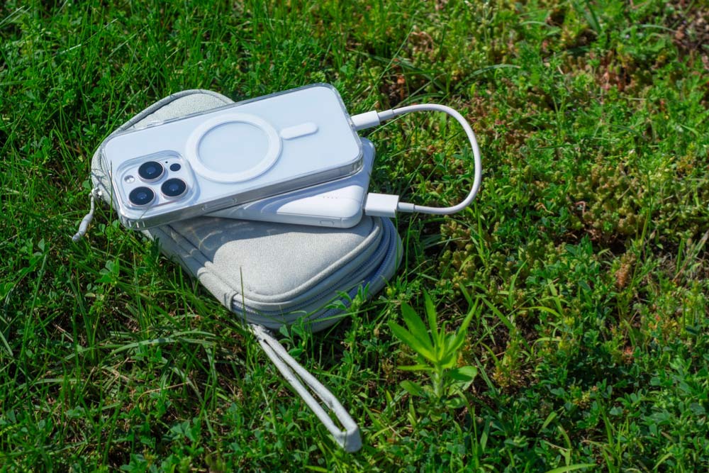 草の上でポータブル充電器につながれたiPhoneと小さなポーチ