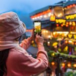 台湾・九份の夜景をスマートフォンで撮影する女性旅行者