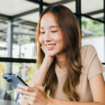 カフェでスマートフォンを見ながら微笑む女性