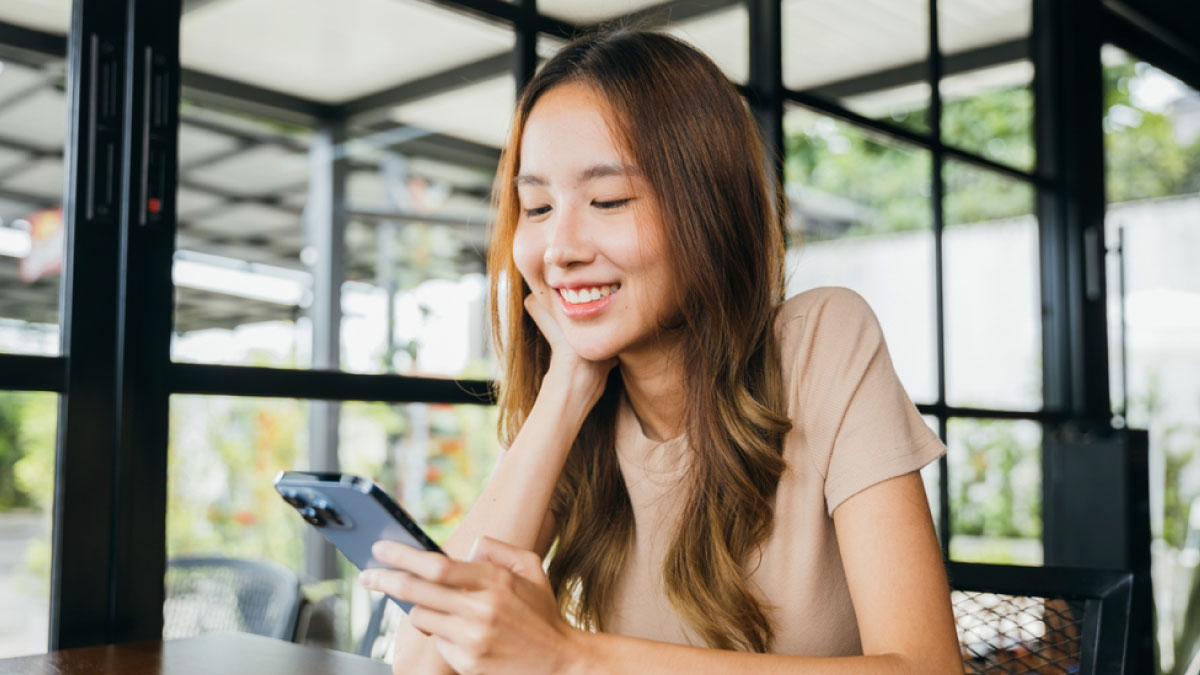 カフェでスマートフォンを見ながら微笑む女性