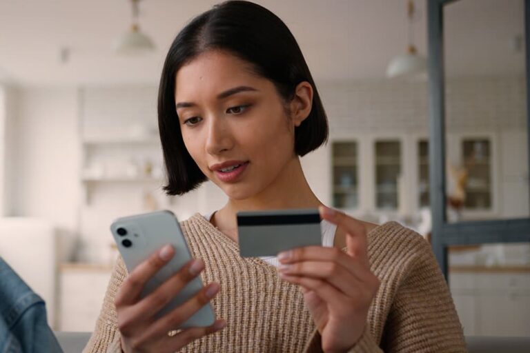 スマートフォンとクレジットカードを手に持ち、eSIMをオンラインで購入・決済する若い女性の様子
