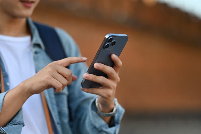 屋外でスマートフォンを手に持ち、画面を指で操作して設定や内容を確認する男性の手元