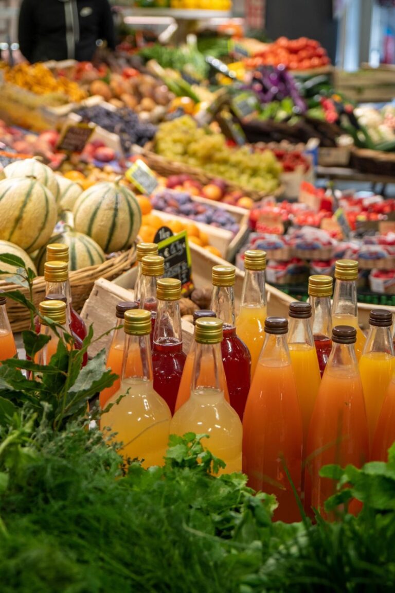 ボルドーの食品市場で、瓶詰めジュースと新鮮な果物や野菜が並ぶカラフルな売り場の風景