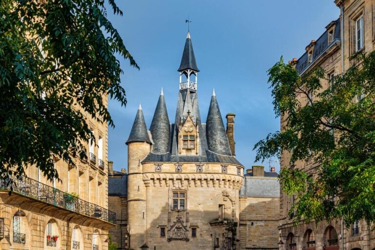 ボルドーのカイヨ門の上部で、中世の趣ある鐘楼と丸みのある尖塔が街並みに映える風景