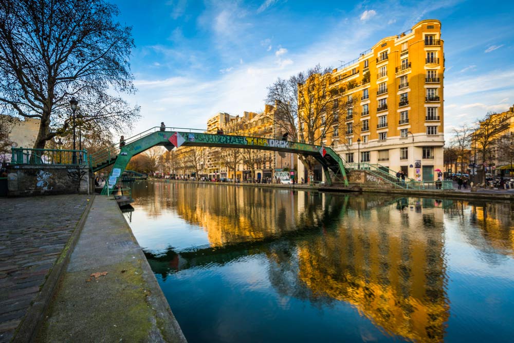 パリのサン・マルタン運河に架かる緑の歩道橋と水面に映る街並みの風景