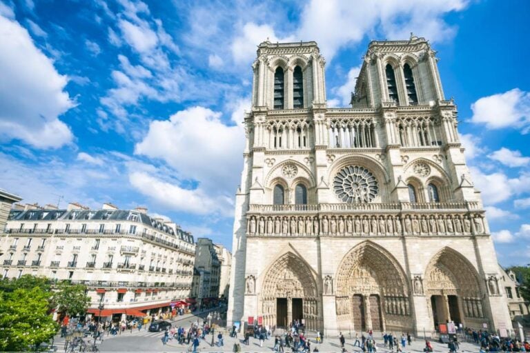 パリ観光の象徴・ノートルダム大聖堂の壮麗な外観と、晴天のもと広場を行き交う観光客の様子
Show less