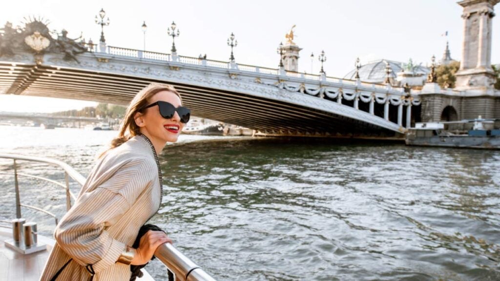 セーヌ川クルーズでパリの街並みを楽しむ女性旅行者の笑顔とアレクサンドル3世橋の風景