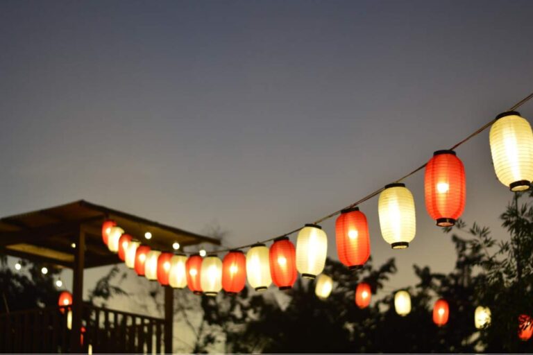 夕暮れの空に赤と白の提灯が並んで灯り、祭りの雰囲気を感じさせる光景