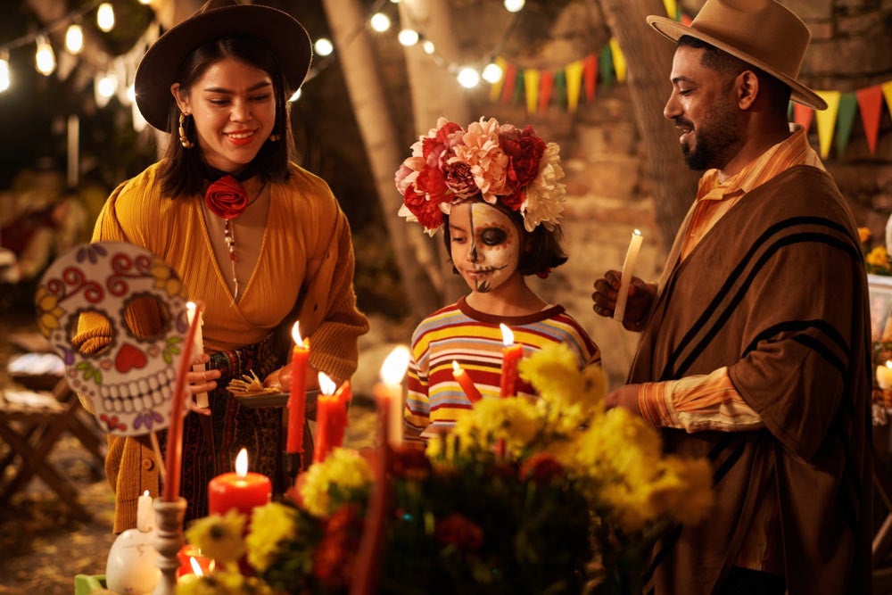 メキシコの死者の日を家族で祝う人々と祭壇に並ぶキャンドルや花の様子