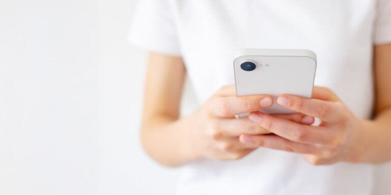 白い背景の前でスマートフォンを両手で持つ人物の手元のクローズアップ