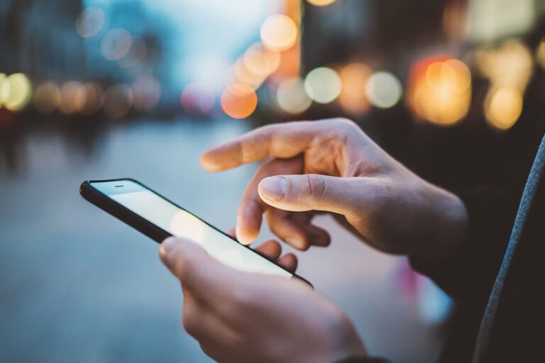 夜の街明かりを背景に、スマートフォンの画面を指で操作してクーポンや情報を確認する手元