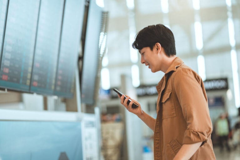 空港でスマートフォンを見ながらフライト情報を確認する旅行者の横顔の様子