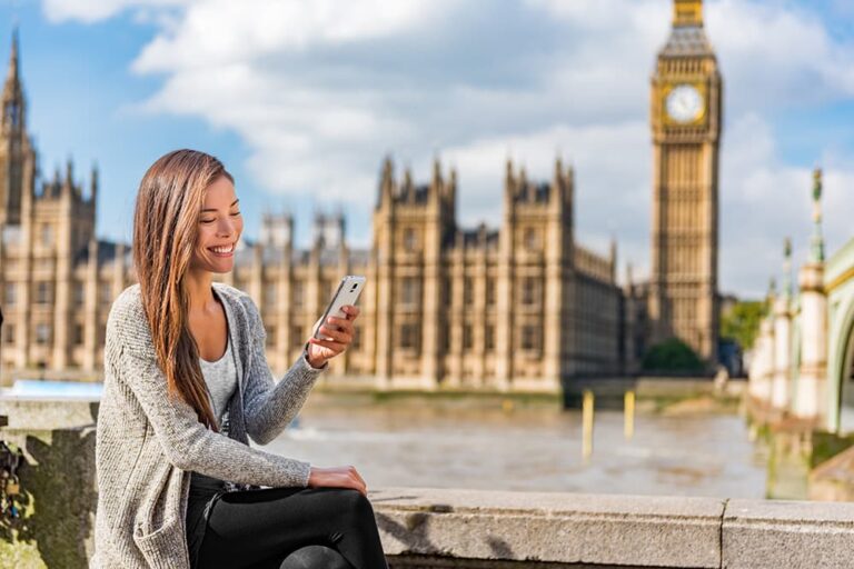 ロンドンのビッグベンを背景に、スマートフォンを快適に使いながら笑顔を見せる女性旅行者