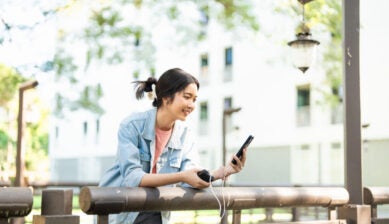 屋外でモバイルバッテリーを使ってスマートフォンを充電しながら楽しそうに操作する女性の様子