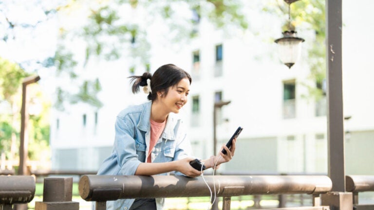 屋外でモバイルバッテリーを使ってスマートフォンを充電しながら楽しそうに操作する女性の様子