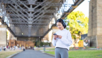 橋の下でスマートフォンを操作しながら音楽を聴くヘッドフォン姿の女性の様子