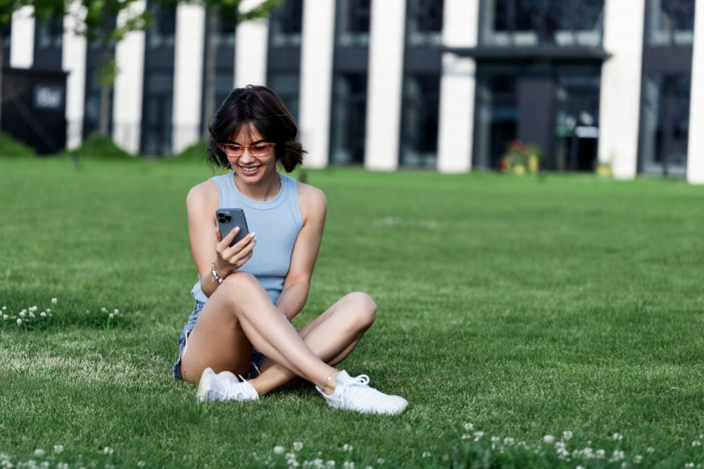 芝生の上に座り、楽しそうにスマートフォンを操作する女性の様子