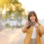 夕方の街中でスマートフォンを構えて写真を撮る女性の様子