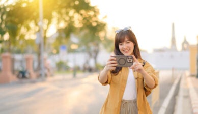 夕方の街中でスマートフォンを構えて写真を撮る女性の様子