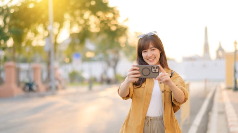夕方の街中でスマートフォンを構えて写真を撮る女性の様子