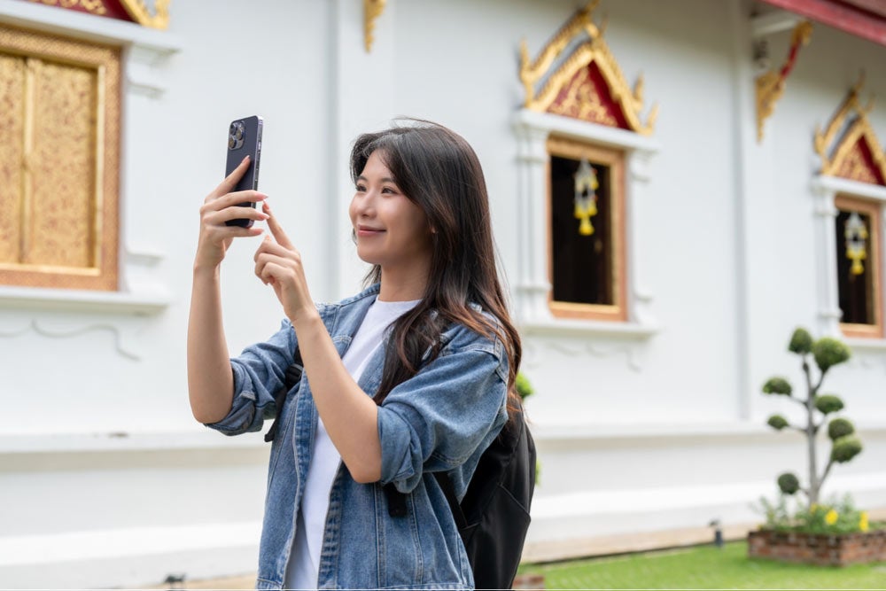 寺院の前でスマートフォンを構えて写真を撮る若い女性