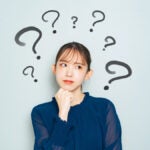 複数のクエスチョンマークに囲まれ、顎に手を当てて考え込む女性の表情