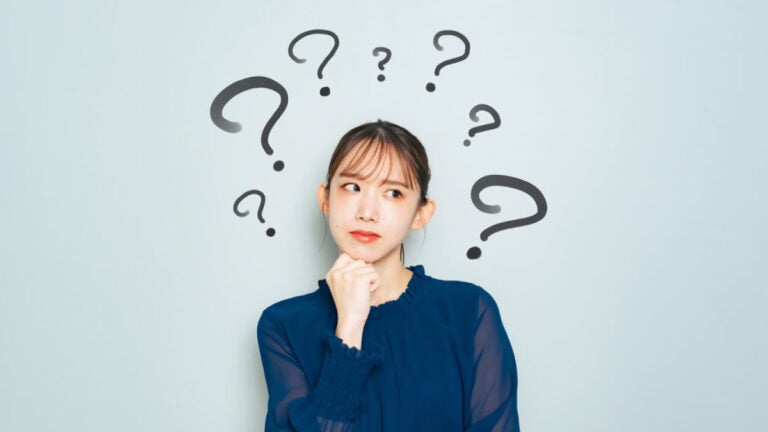 複数のクエスチョンマークに囲まれ、顎に手を当てて考え込む女性の表情