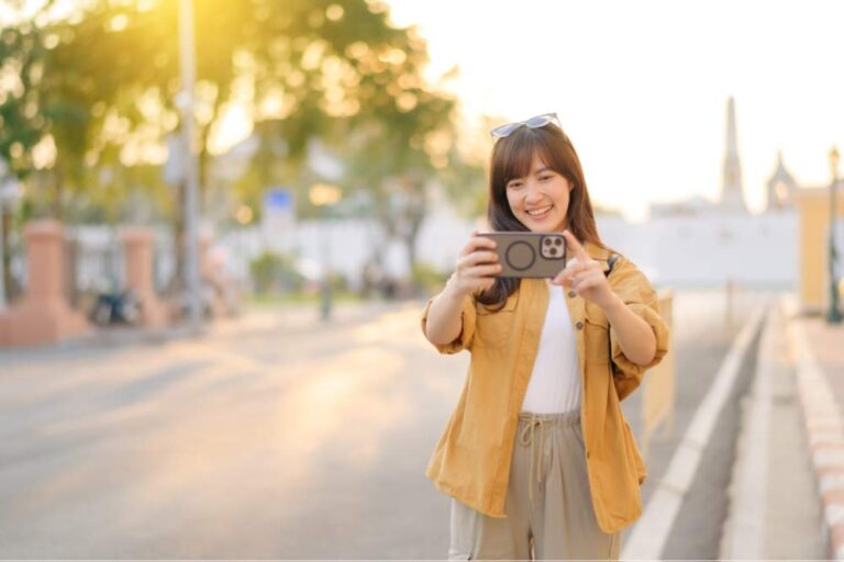 夕陽に照らされた街角で、スマートフォンを手に笑顔で自撮りをする女性の様子