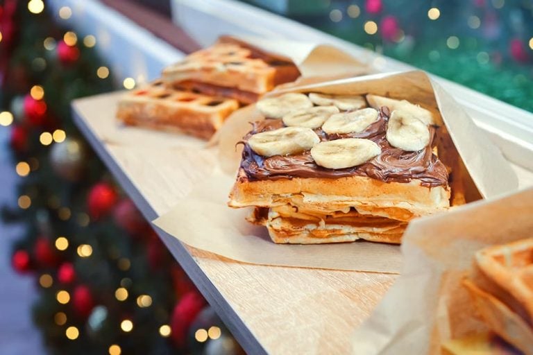 クリスマスのイルミネーションを背景に屋台に並ぶ、食べ歩きにぴったりのチョコレートとバナナがたっぷり乗ったベルギーワッフル