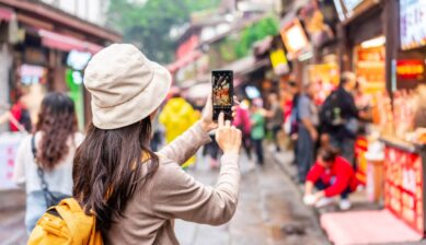 中国の賑やかな街並みで、観光客がスマートフォンを使って屋台や通りの様子を撮影している風景