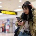 空港でスマートフォンを見ながら、通信が繋がらず困っている旅行者の様子