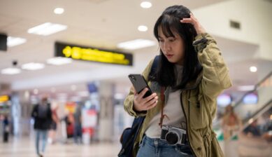 空港でスマートフォンを見ながら、通信が繋がらず困っている旅行者の様子
