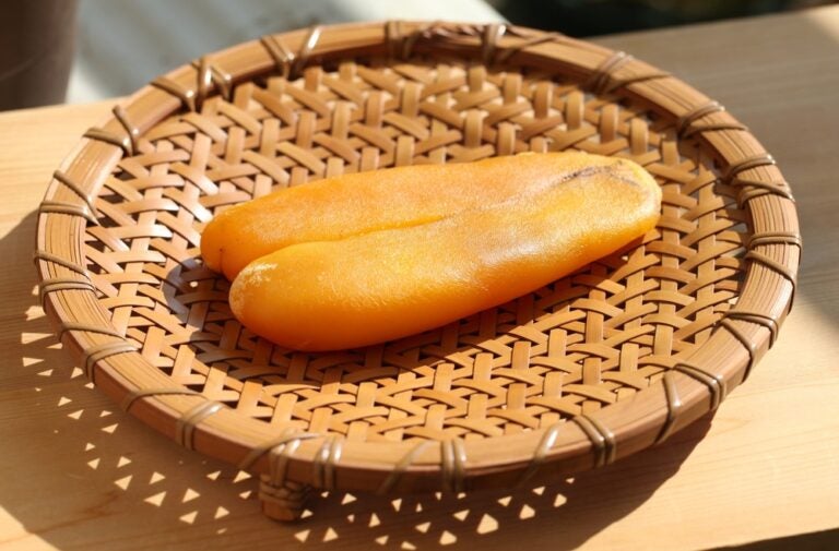 台湾お土産として人気の高級珍味、からすみ。鮮やかなオレンジ色をしたツヤのあるからすみ一腹が、竹編みのザルの上に置かれ、日の光を浴びている様子