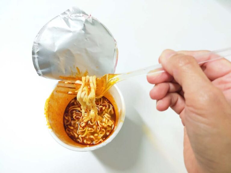 カップ麺のフタを開け、フォークで麺を持ち上げて食べている様子の写真