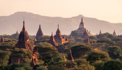 ミャンマーのバガン遺跡群に立ち並ぶパゴダと寺院を、夕暮れの柔らかな光と山並みを背景に望む風景