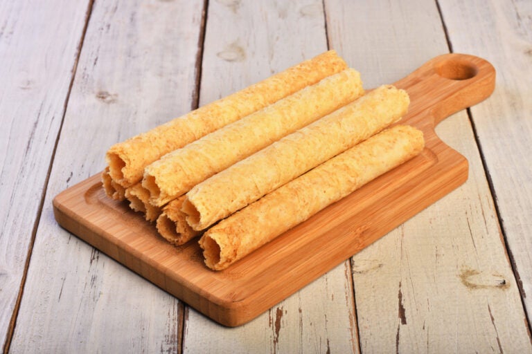 台湾お土産として定番のエッグロール。サクサクとした薄焼き生地を何層にも巻いた筒状のクッキーが、木製のカッティングボードの上に重ねて置かれた様子