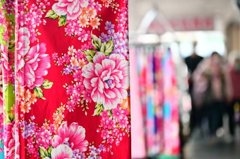 台湾お土産のポーチや小物で人気の台湾花布。鮮やかな赤地に大輪のピンクの牡丹などが描かれた伝統的な生地が、市場の店頭に吊るされている様子